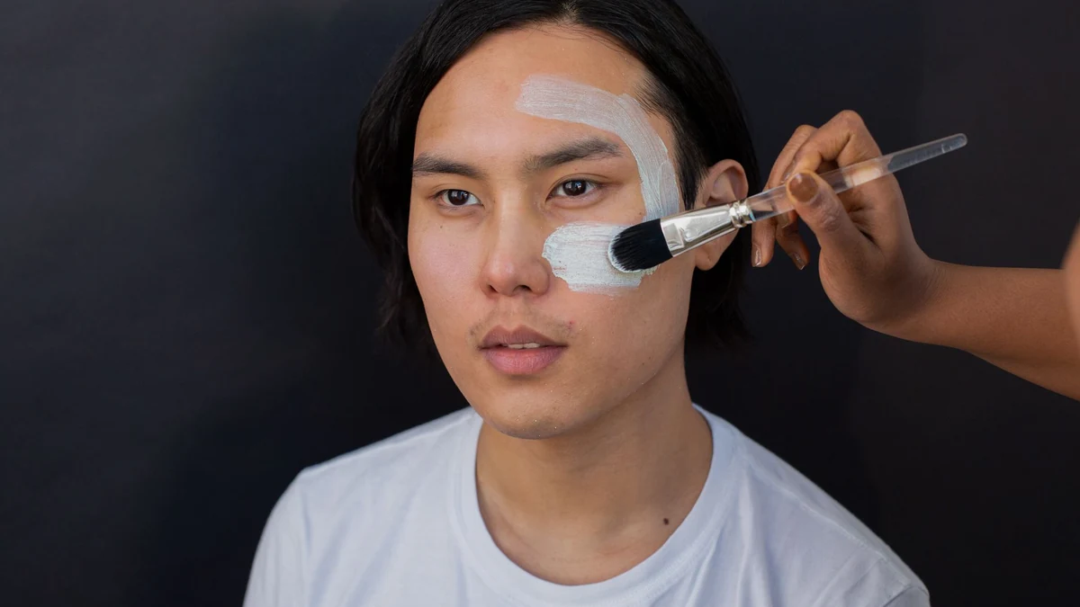 Cosmetologist using cosmetic brush to apply exfoliating peeling solution on patient forehead and cheek