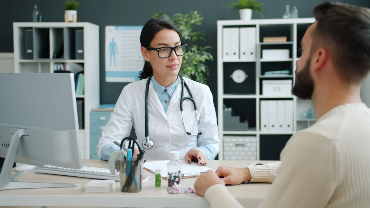 Female doctor in white lab coat and stethoscope consulting with male patient across clinic desk
