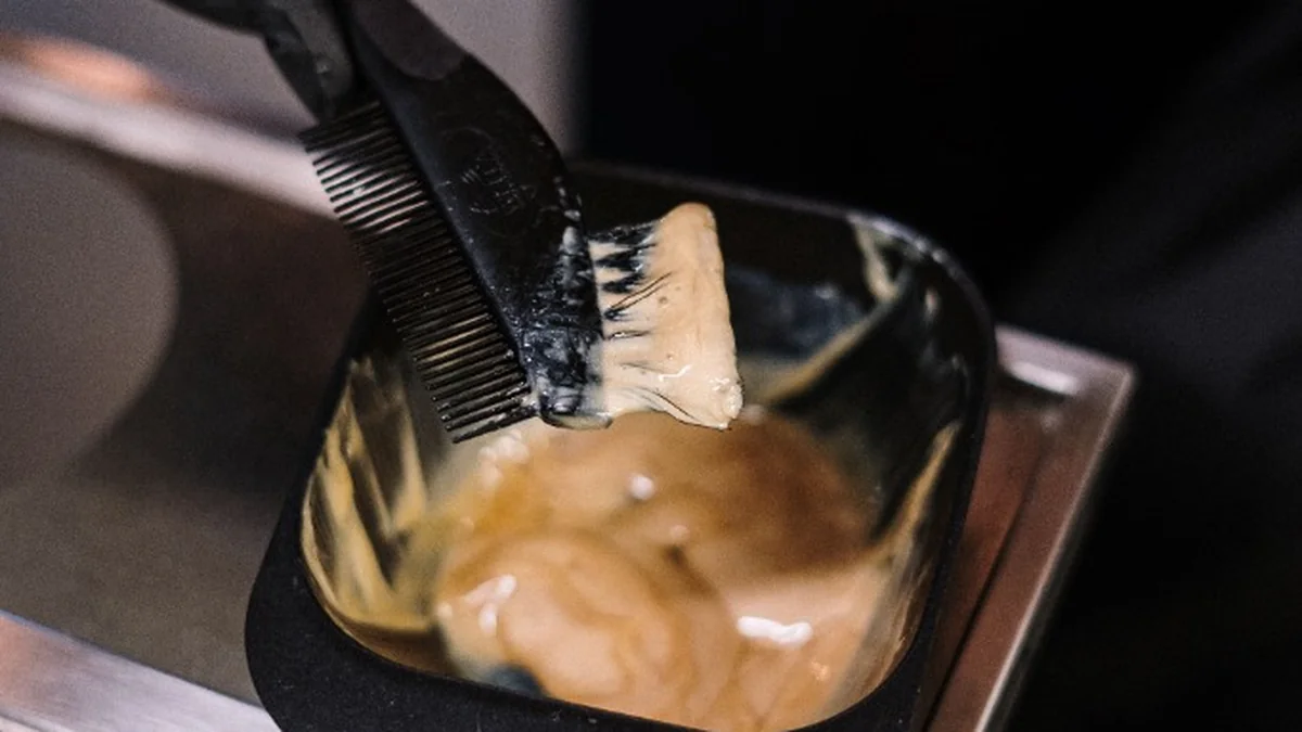 Stylist dipping dual-sided tint brush into creamy keratin smoothing treatment formula in applicator bowl