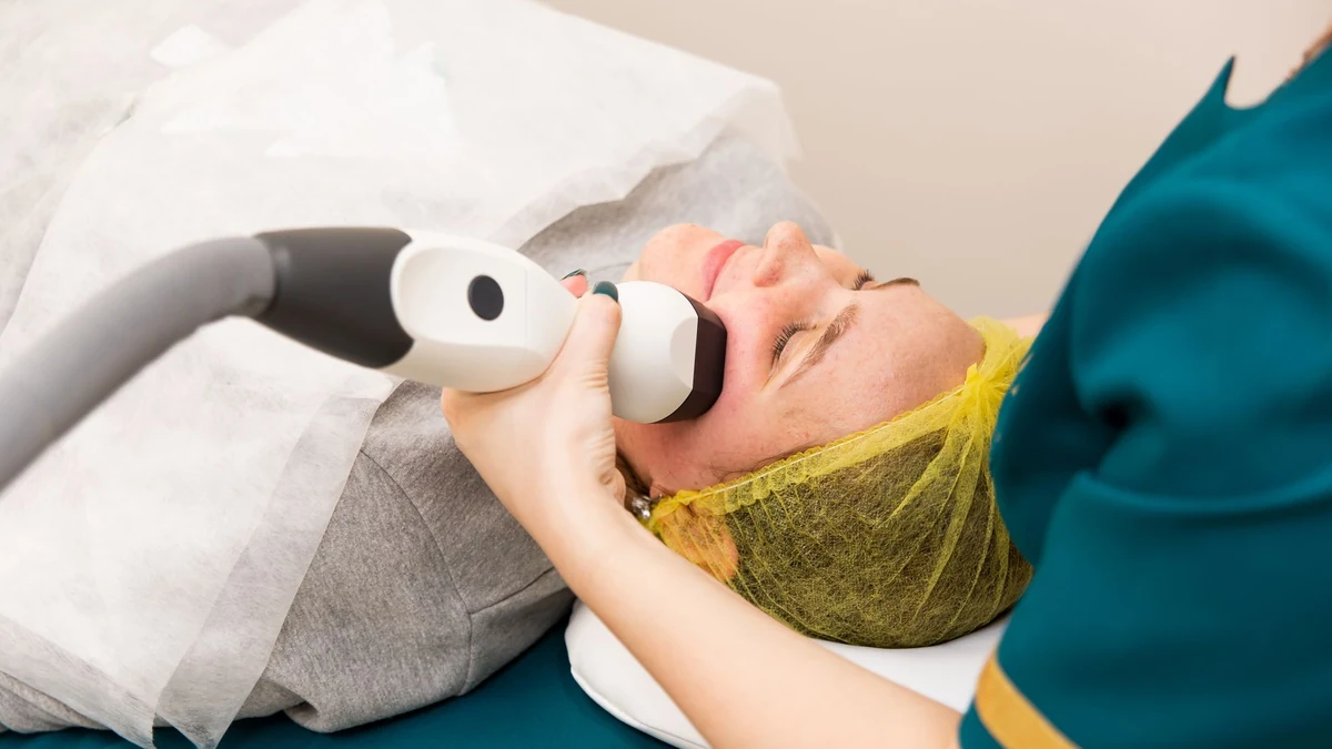 Patient undergoing medical laser skin toning procedure with protective hairnet and cooling handpiece