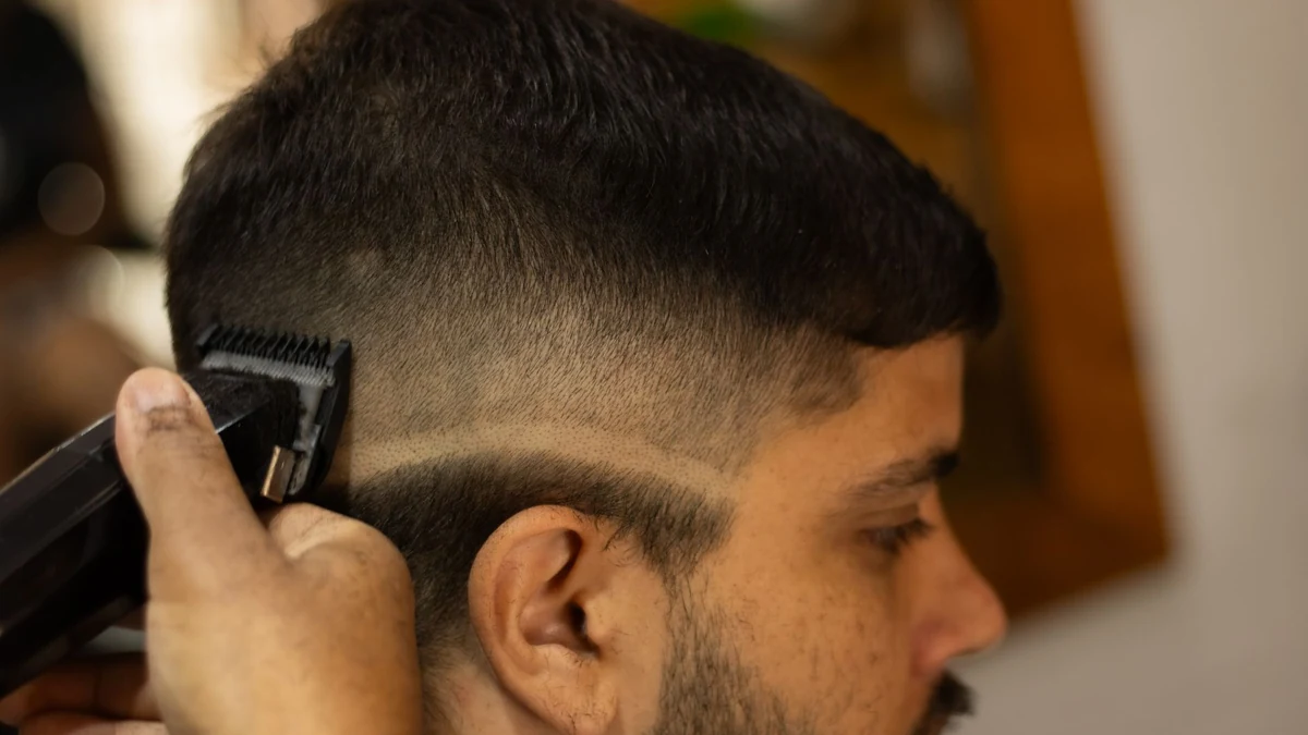 Barber performing a clean high skin fade with electric clippers on man with dark curly hair