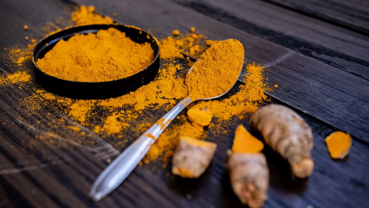 Golden turmeric powder in black dish with silver spoon and fresh turmeric rhizome slices on rustic dark wood