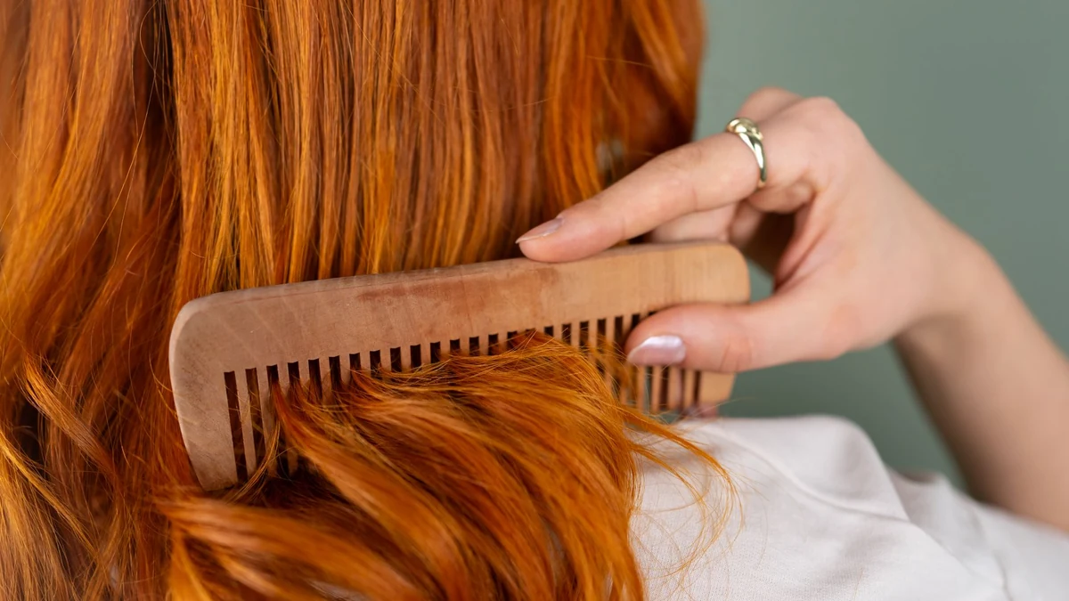 Woman gently detangling smooth hydrated hair with wide-tooth wooden comb