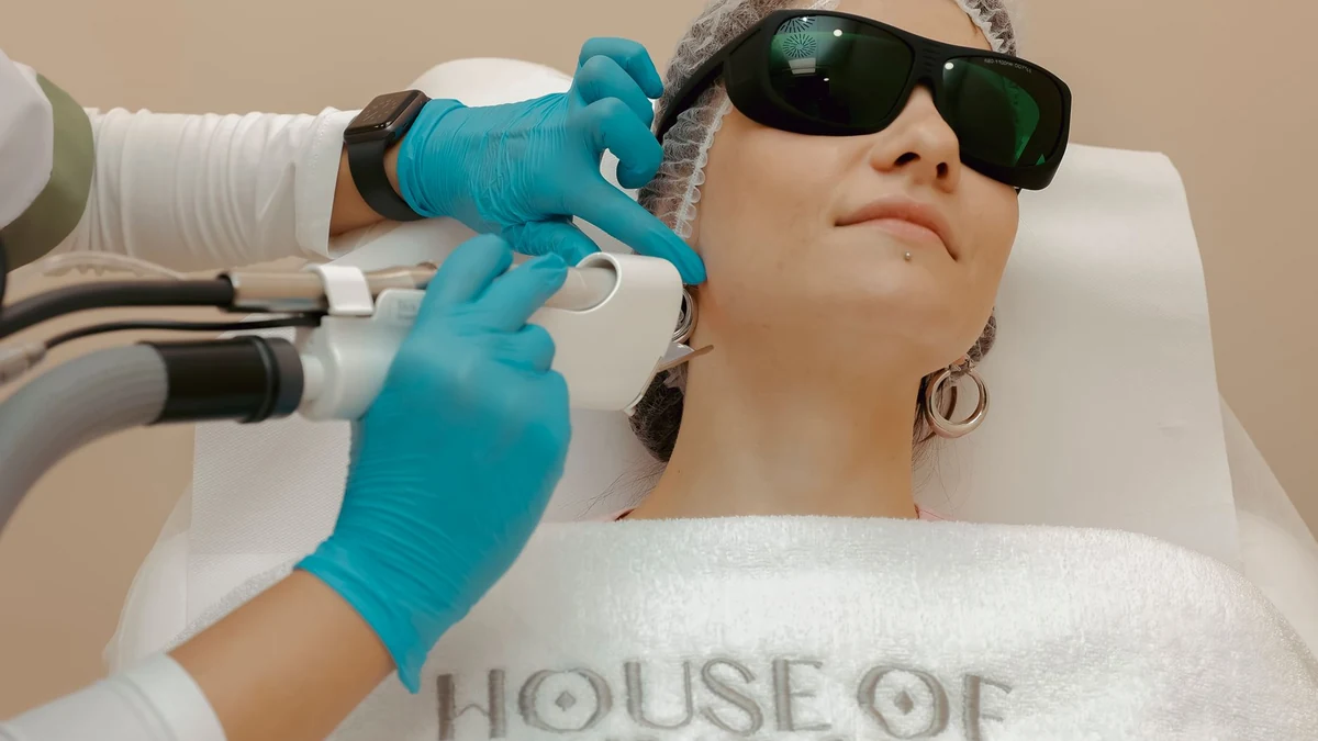 Dermatologist applying precision aesthetic laser handpiece near patient periorbital area with protective eyewear