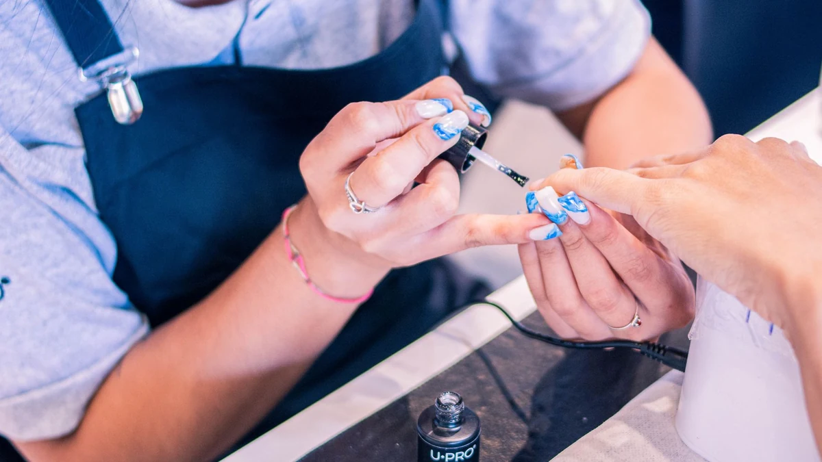 Nail artist applying soft gel extension tips adhering gently over the natural nail plate