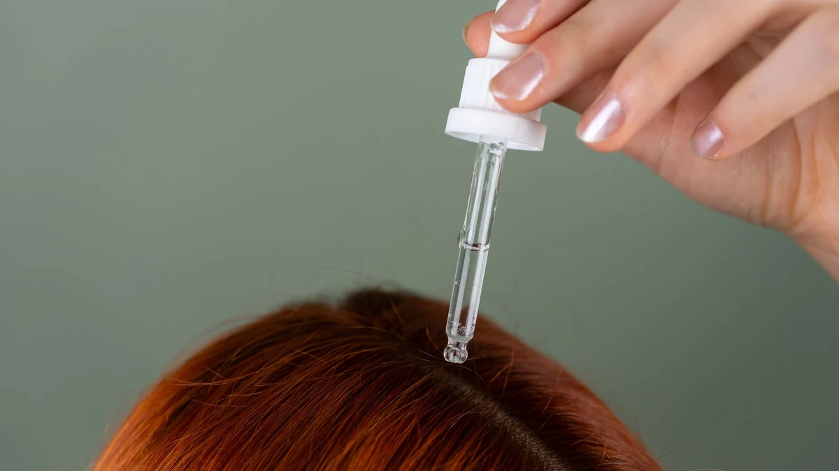 Precision glass dropper dispensing nourishing botanical oil directly onto clean scalp parting